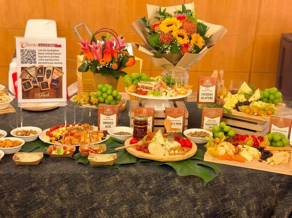 A cheese tasting spread with labelled cheese boards, grapes, nuts, fruit skewers and floral arrangements